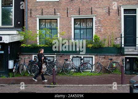 Femme marche sur le trottoir, vêtus de noir avec de nombreux vélos stationnés sur l'arrière-plan Banque D'Images