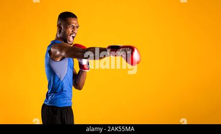 Prêt pour le combat. Homme noir agressif pratiquer la boxe poinçons en gants, fond jaune. Panorama, copyspace Banque D'Images