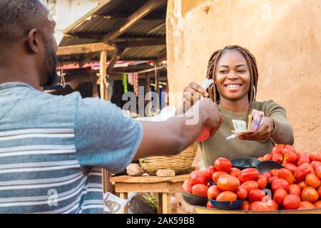 Fille noire vente de tomates dans un marché africain à un client de sexe masculin de sourire et de se sentir heureux et satisfaits Banque D'Images