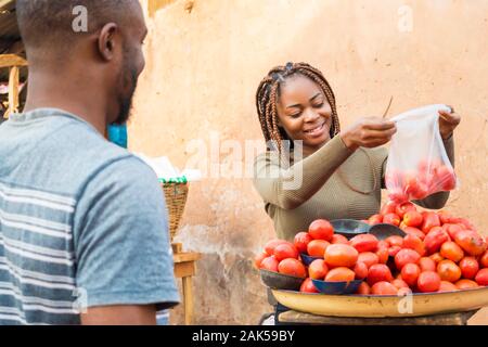 Fille noire vente de tomates dans un marché africain à un client smiling Banque D'Images