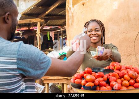 Fille de l'Afrique de vendre des tomates dans un marché africain à un client de sexe masculin de sourire et de se sentir heureux et satisfaits Banque D'Images