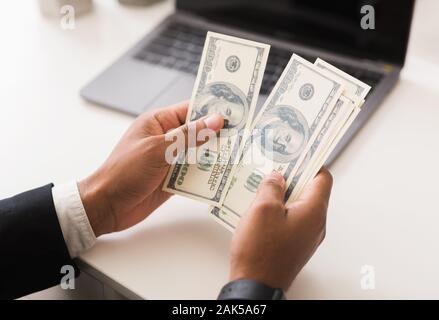 Mains d'afro businessman comptant des billets de dollar en face de laptop in office, Close up, concept de revenu d'entreprise Banque D'Images