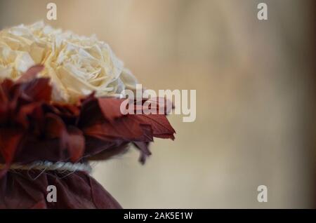 La moitié d'un bouquet décoratif artificiel blanc de roses, à l'horizontale en bourgogne feuilles sur un fond clair. Banque D'Images