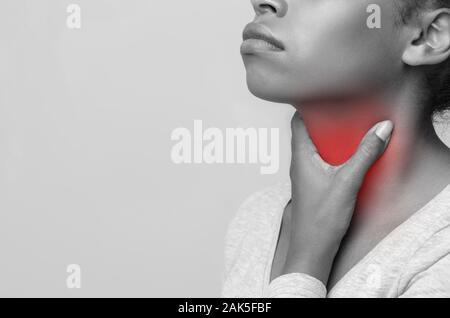 Photo monochrome de femme africaine souffrant d'amygdalite, effleurant sa mis en évidence avec la gorge rouge, recadré, l'espace libre Banque D'Images