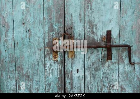 Verrou porte rouillée et d'un cadenas de verrouillage coulissant sur old weathered barrière en bois avec peinture bleue écaillée. Banque D'Images