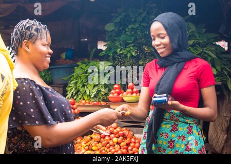 Portrait d'une femme africaine La vente de denrées alimentaires dans un marché africain tenant un dispositif de point de vente mobile la collecte d'une carte de crédit à partir d'une coutume Banque D'Images