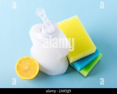 Vue de dessus sur blanc du liquide vaisselle dans une bouteille en plastique, mousse de citron et trois éponges. Pureté et produits chimiques ménagers. Cuisine détergent sur un bleu. Banque D'Images