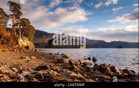 Le soleil brille sur les rochers et d'arbres sur les rives du Derwent Water en Angleterre du Lake District. Banque D'Images