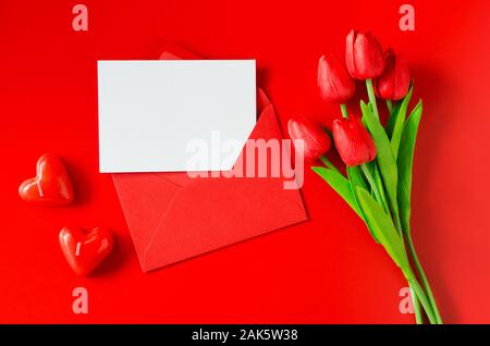 Carte de souhaits pour la Saint-Valentin, la Journée de la femme ou la Fête des Mères. Enveloppe rouge avec du papier blanc, bouquet de tulipes et de bougies en forme de coeur. Vue supérieure de la wi Banque D'Images