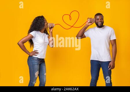 Belle black girl in aime parler par téléphone peut avec son petit ami, l'amour est dans l'air, jaune fond studio, l'espace vide Banque D'Images