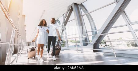 Prêt pour une lune de miel. Plan large de happy black couple en train de marcher avec des valises à l'aéroport, low angle view, bannière horizontale, panorama Banque D'Images