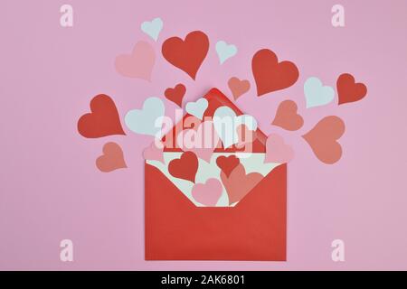 Lettre ouverte de blanc vide enveloppe rouge avec beaucoup de rouge, rose et blanc qui sort des coeurs en papier répartis sur fond rose comme lettre d'amour Banque D'Images