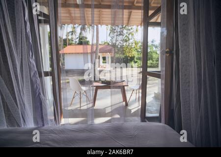 Hébergement de luxe à destination tropicale. Selective focus on moustiquaire dans la chambre du bungalow avec vue sur jardin. Banque D'Images