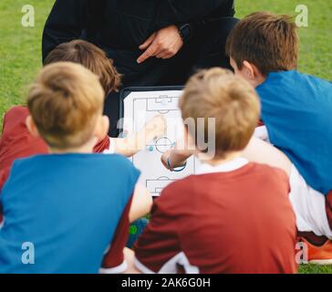 Coach d'enseigner aux enfants sur la formation du football. Les jeunes garçons assis ensemble avec l'entraîneur sur le terrain d'herbe. Stratégie d'apprentissage des enfants à l'aide de tact entraîneur de soccer Banque D'Images