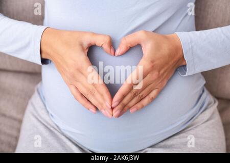 La grossesse. Méconnaissable pregnant woman Holding Hands On Belly formant une forme de coeur. Vue de dessus, Cropped Banque D'Images