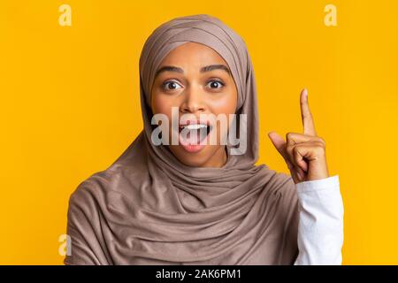 Eureka. Excitée Black Girl in Hijab avoir Idée, doigt pointé vers le haut, s'Problème/Solution, Fond jaune avec de l'espace libre, libre Banque D'Images