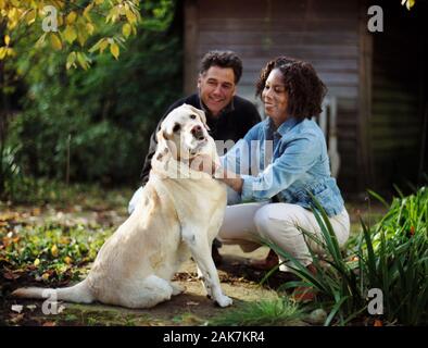 Happy mid-adult couple tapotant leur chien dans la cour arrière de leur maison. Banque D'Images