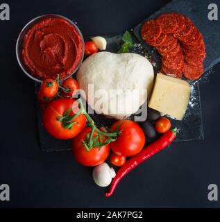 Pâte crue pour la pizza avec des ingrédients et des épices sur l'arrière-plan du tableau noir en forme de coeur aime la nourriture de Valentines Day concept Banque D'Images