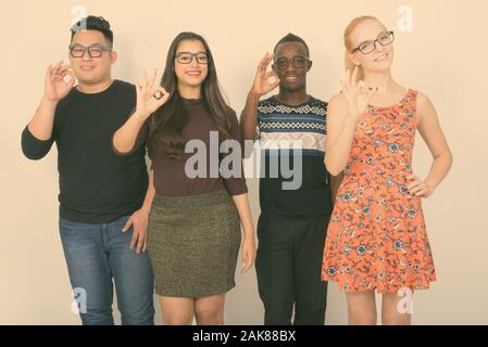 Studio shot of happy groupe diversifié de multi ethnic friends smiling tout en donnant à l'ensemble lunettes signe ok Banque D'Images