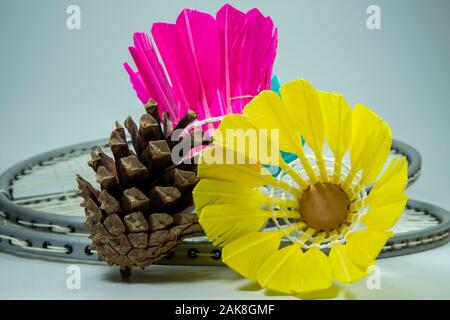 Raquettes de badminton et coloré, rose et jaune volants de plumes naturelles placées sur la surface gris avec cône de pin et vue en gros plan. Sport amateur Banque D'Images