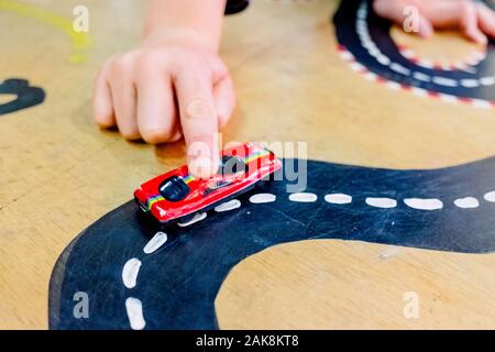 Enfant joue avec deux voitures miniatures dans un jouet circuit. Banque D'Images