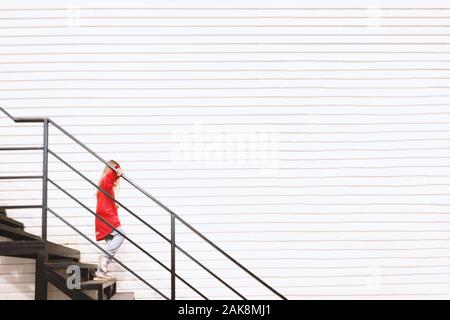 Fille avec des lunettes de soleil et veste rouge descend les escaliers noirs près de mur blanc. Passez du temps à l'extérieur. Enfant jouant à l'extérieur à l'automne. L'enfance memorie Banque D'Images