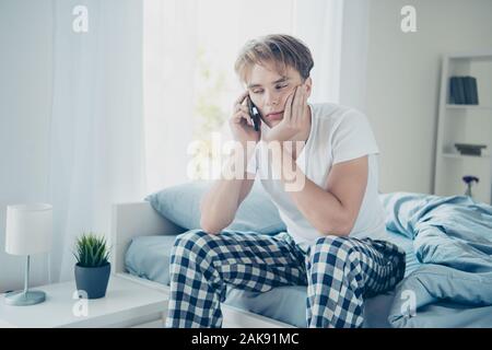 Portrait de fatigué épuisé blonde brun s'asseoir sur l'utilisation de lit portable appeler sa femme après une dure partie sentir gueule maux dans l'usure à l'intérieur de la chambre Banque D'Images