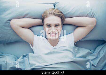 Haut haut au-dessus de l'angle positif photo joyeux guy lying on bed sentir éveillé confort douillet d'une bonne nuit de sommeil dans l'intérieur de la chambre le matin Banque D'Images