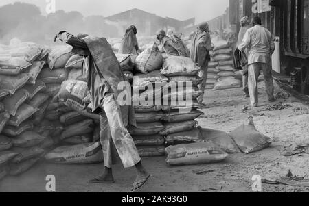 Équipe de travailleurs masculins dans des conditions poussiéreuses déplacer de gros sacs de ciment d'entraîner dans des conditions chaudes de l'été à Mathura, Uttar Pradesh, Inde. Banque D'Images