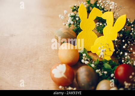 Les oeufs de pâques, élégant lapin jaune dans nid de fleurs de printemps sur table en bois rustique, de l'espace pour le texte. Les oeufs de pâques teints naturels et décorations sur lapin Banque D'Images