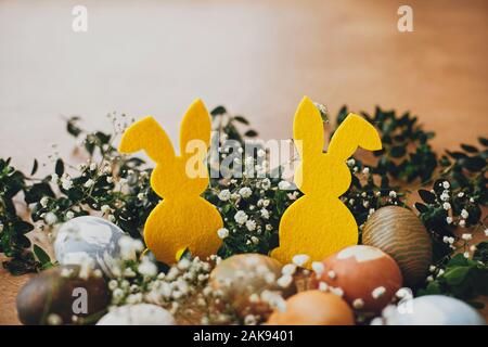 Les oeufs de pâques, élégant lapin jaune dans nid de fleurs de printemps sur table en bois rustique, de l'espace pour le texte. Les oeufs de pâques teints naturels et décorations sur lapin Banque D'Images