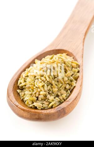 Tas de matières premières, non cuites ou rôties freekeh firik, grain de blé, en cuillère en bois sur fond blanc avec selective focus Banque D'Images