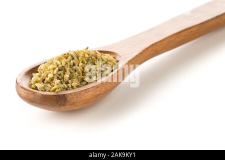 Tas de matières premières, non cuites ou rôties freekeh firik, grain de blé, en cuillère en bois sur fond blanc avec selective focus Banque D'Images