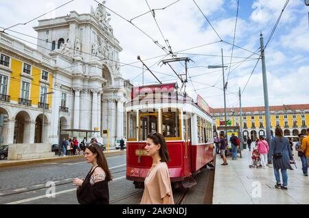 Lisbonne, Portugal : Deux jeunes femmes devant un vieux tramway rouge à côté de la Rua Augusta de Triomphe à la place Praça do Comércio. Banque D'Images