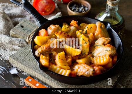 Dîner de Thanksgiving. Compote de pommes de terre avec des ailes de poulet, tomates et épices, servi dans une poêle en fonte sur une table rustique. Banque D'Images