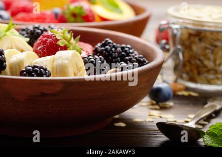Fruit sain muesli avec banane fraise amandes et blackberry dans l'argile plat sur table de cuisine en bois Banque D'Images