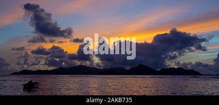 La silhouette du bateau de pêche en mer au coucher du soleil avec en arrière-plan l'île de Praslin, La Digue, Seychelles Banque D'Images