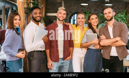 Groupe de jeunes de l'équipe de créateurs de succès qui pose à l'appareil photo dans office, panorama Banque D'Images