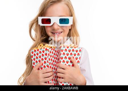 Une petite fille aux longs cheveux blonds et de maquillage, les lunettes 3D ressemble film ou cartoon avec le pop-corn isolé sur fond blanc Banque D'Images