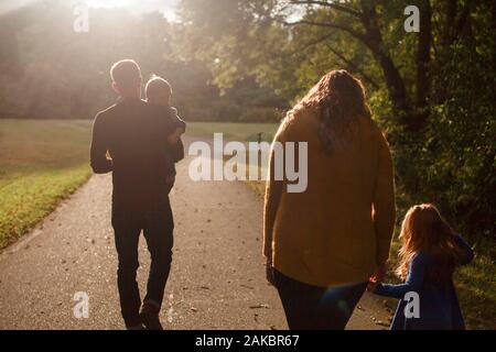 Une famille marche ensemble en tenant les mains dans un parc au soleil couchant Banque D'Images