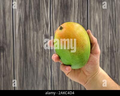 Male hand holding mangue fraîche sur fond de bois Banque D'Images