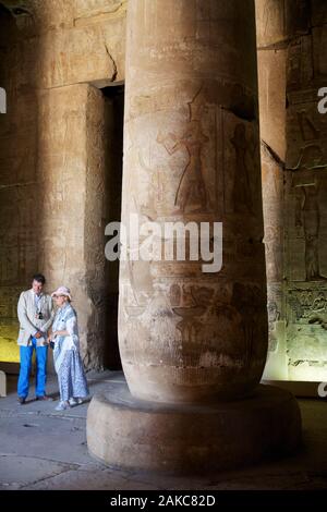 L'Égypte, de la Haute Égypte, vallée du Nil, Dendérah, tourist couple élégamment vêtue en bas des colonnes de la salle hypostyle du temple d'Hathor Banque D'Images