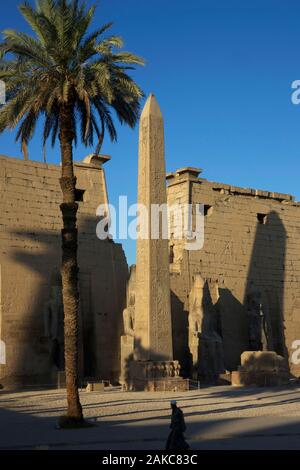 L'Égypte, de la Haute Égypte, vallée du Nil, Luxor, gardien en passant en face de la façade de temple de Louxor avec ses statues de Ramsès II, l'obélisque et grand palmier Banque D'Images