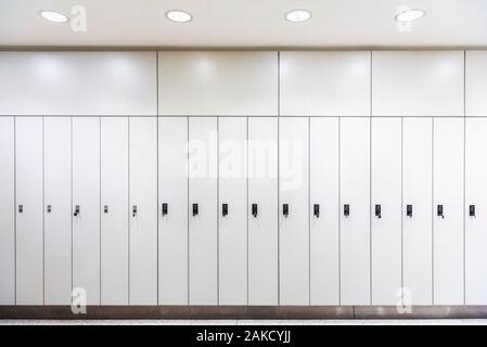 Curieux de luxe dans une rangée, sous lumière artificielle. Meubles en métal blanc. Un vestiaire avec des casiers blancs. Retour au contexte scolaire. Vestiaire intérieur. Banque D'Images