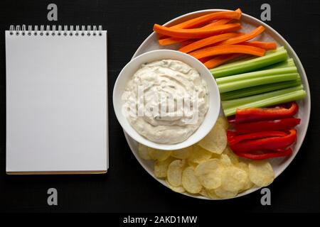 Des oignons caramélisés Trempette avec des croustilles de pommes de terre, légumes et le bloc-notes en blanc sur fond noir, vue du dessus. Mise à plat, les frais généraux, d'en haut. Savs copie Banque D'Images