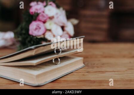 Deux anneaux de mariage dans un livre et de bouquet de mariage sur la table. Banque D'Images