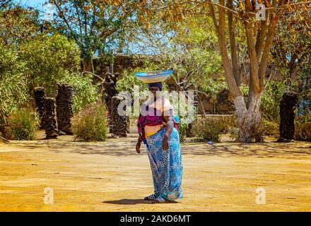 Gorée, Sénégal, 22 avril 2019 : Le Sénégal femme non identifiée a un panier de fruits sur la tête et portant les vêtements traditionnels colorés Senegl typique. Banque D'Images