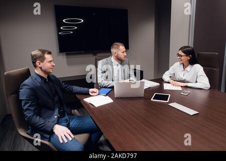 Jeune entreprise, l'entreprise créative des gens de différentes races et de l'âge se rassembler dans une salle de réunion dans l'intérieur de bureau moderne sombre, vivously à discuter. Banque D'Images