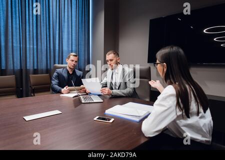 Jeune entreprise, l'entreprise créative des gens de différentes races et de l'âge se rassembler dans une salle de réunion dans l'intérieur de bureau moderne sombre, vivously à discuter. Banque D'Images