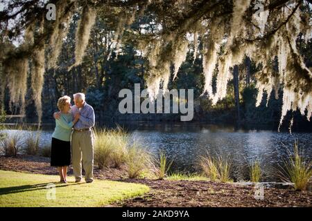 Happy senior couple walking fermer ensemble près d'un lac. Banque D'Images